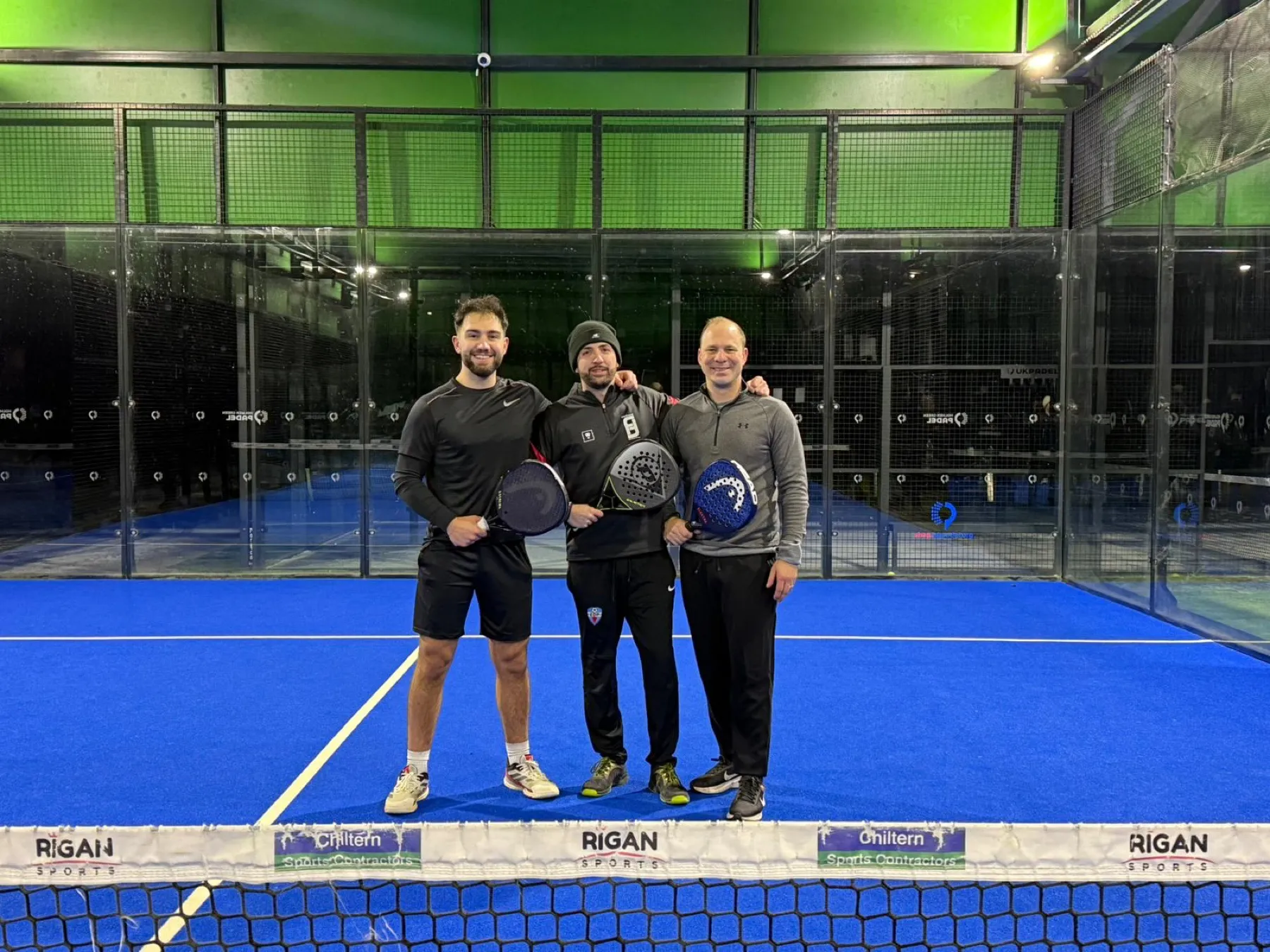Three players together on a padel court, rackets in hand.