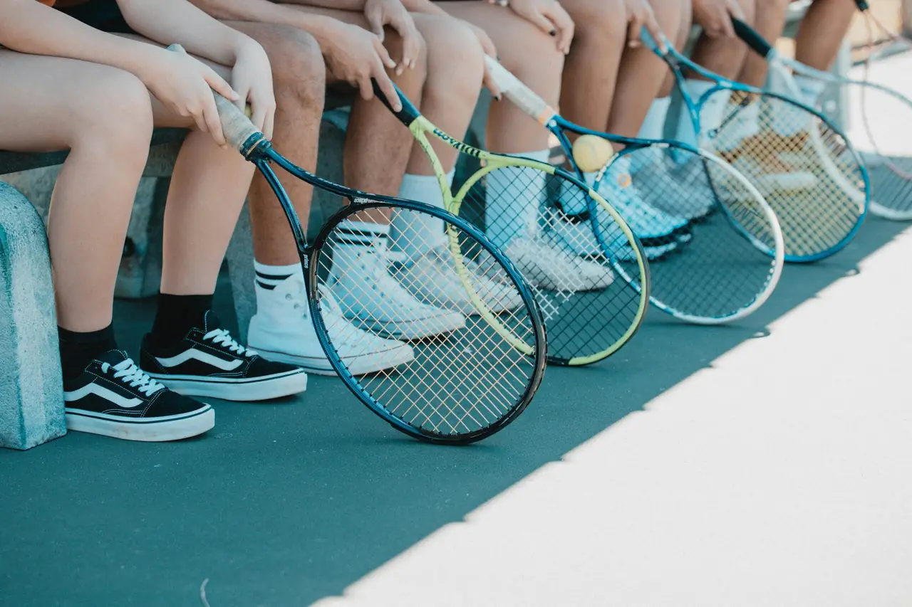 A row of players sitting courtside with their rackets, waiting to go on.