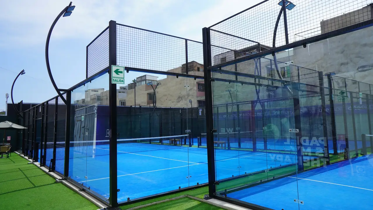 An outdoor padel court in daylight: glass at the back, mesh above.