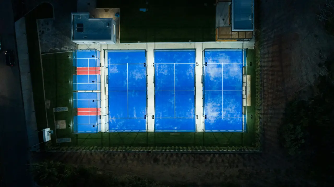 Two padel courts seen from directly above at night, lit from the inside.