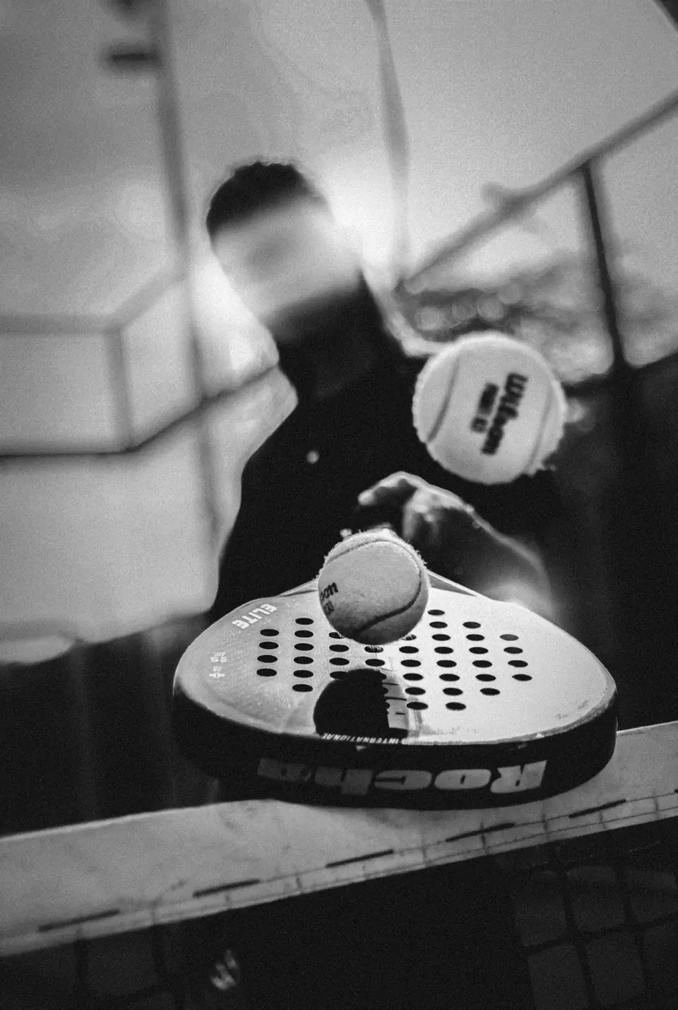 A padel racket meeting the ball, in black and white.