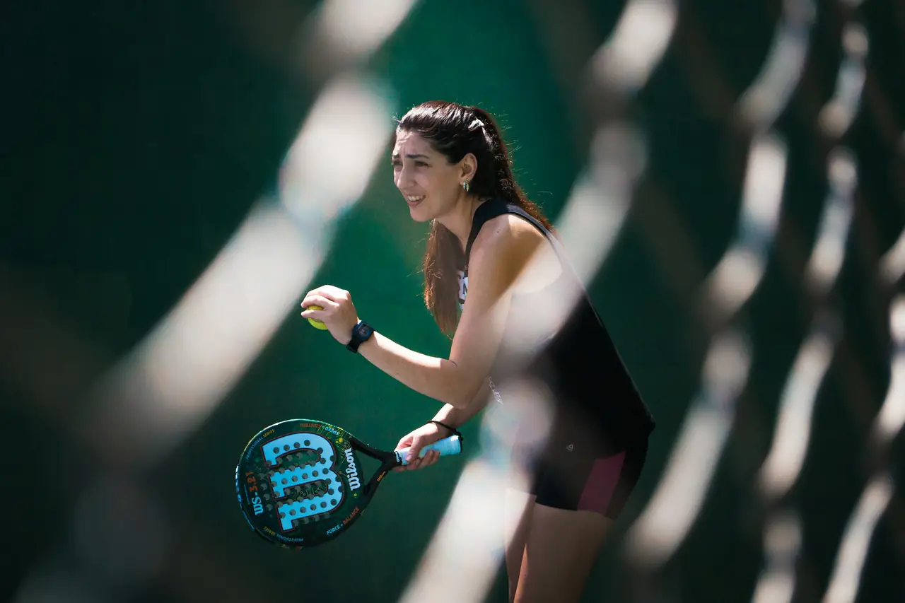 A player waiting to serve, seen through the mesh of the court wall.